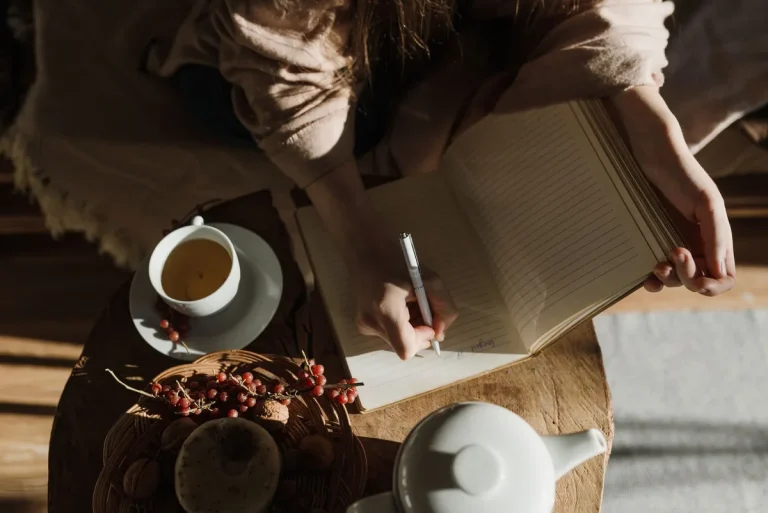 Personne assise à un bureau écrivant dans un carnet, lumière douce naturelle, moment de réflexion calme