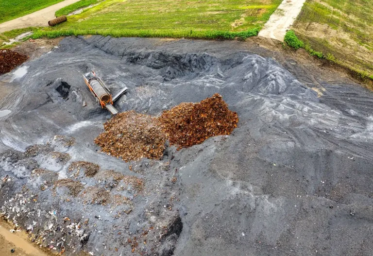Mains de jardinier superposant des matières organiques dans un bac de compostage avec déchets verts