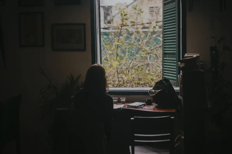 Personne assise près d'une fenêtre, calme et sereine, pratiquant la pleine conscience et la détente