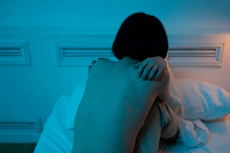 Personne seule assise sur un lit dans une chambre sombre, exprimant le stress et les troubles du sommeil.