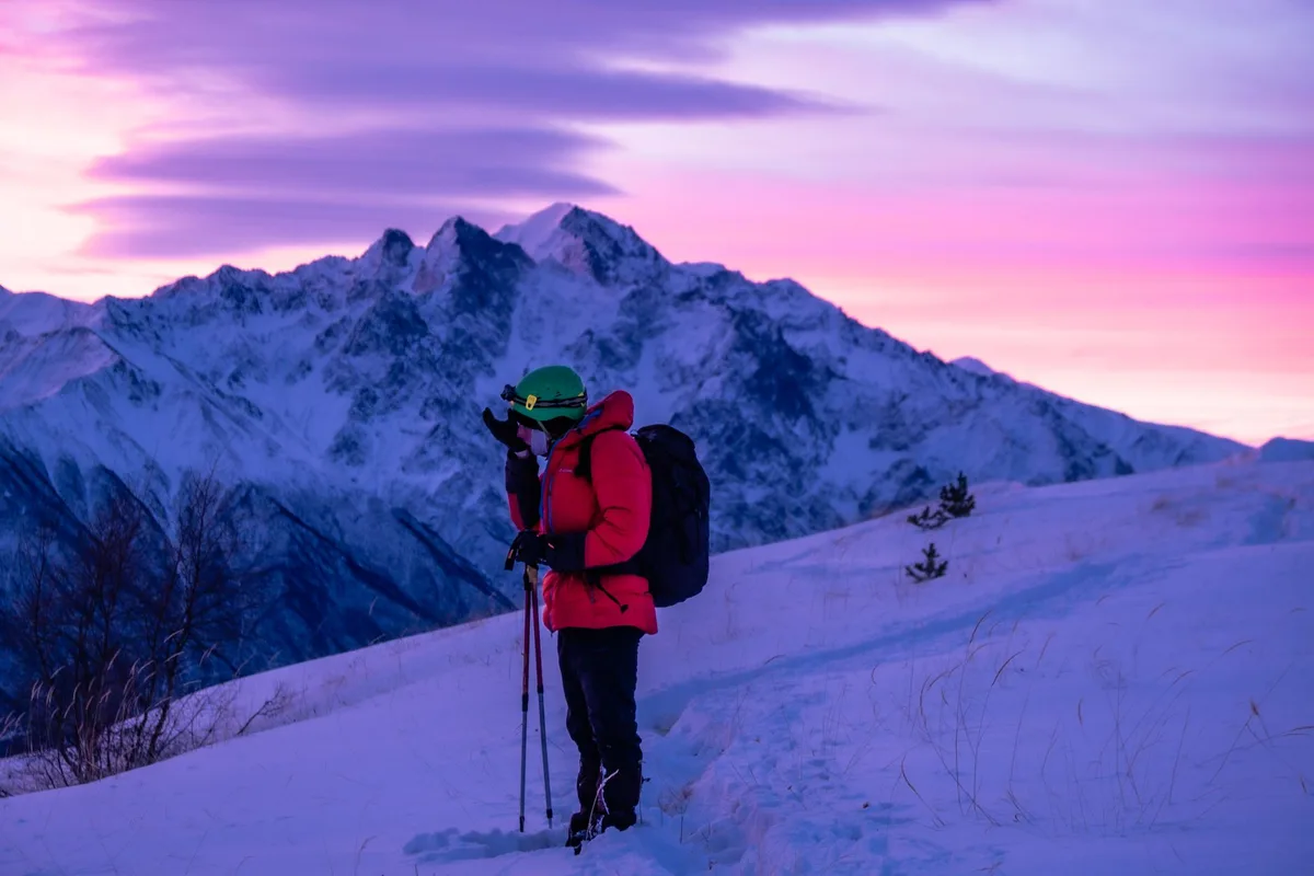 Randonneur équipé d'une veste chaude observant le lever de soleil en montagne