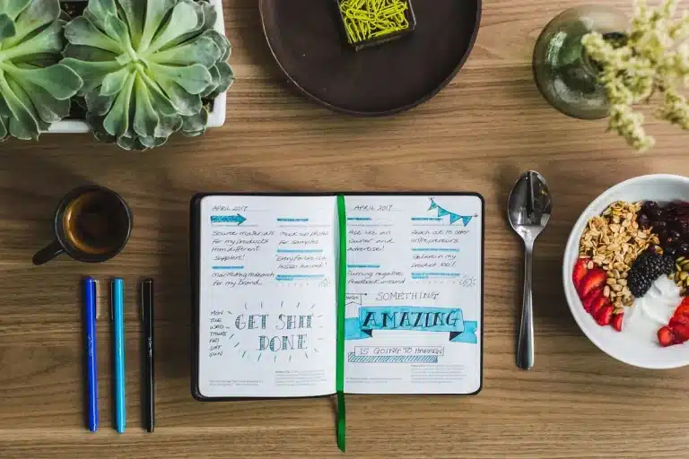 Personne anonyme écrivant dans un carnet près d'une fenêtre ensoleillée, tasse de café à côté